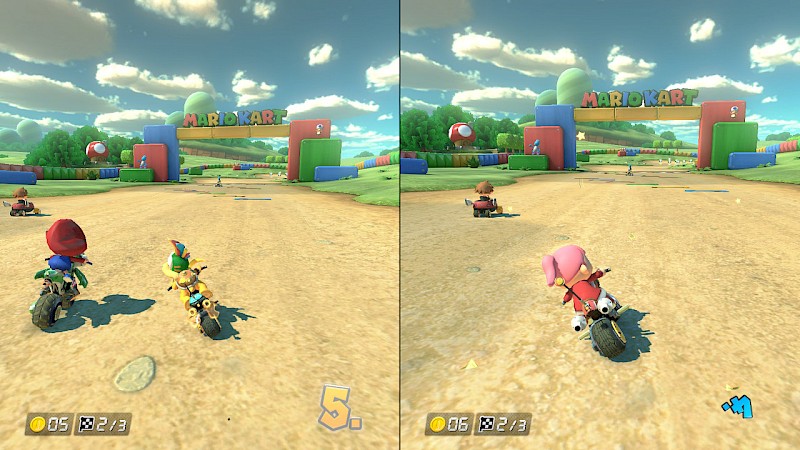 Ein Screenshot von Mario Kart. Er zeigt den geteilten Bildschirm im Zweispieler-Modus. Beide fahren auf das Zieltor zu. Die Landschaft besteht aus einem Sandweg, grünen Hügeln und blauem Himmel.
