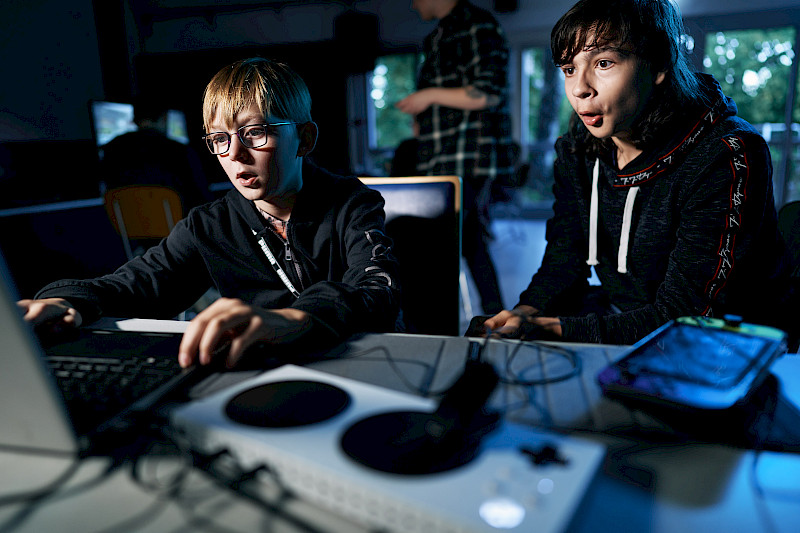 Zwei Jugendliche spielen mit einem Laptop. Zum Steuern nutzen sie Controller. Vorne ist ein Xbox Adaptive Controller.