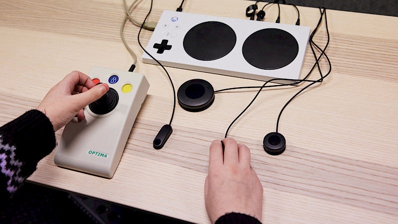 Eine Jugendliche steuert ein Spiel mit dem Adaptive Controller. Sie nutzt auch Buttons und einen Stick von Optima.