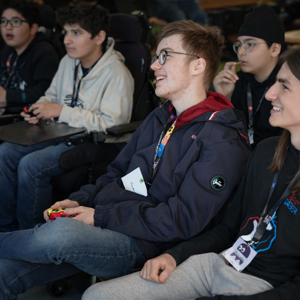 Mehrere Jugendliche sitzen zusammen und spielen ein Videospiel. Sie halten Controller in der Hand und haben Spaß. Einige lachen und schauen auf den Bildschirm.